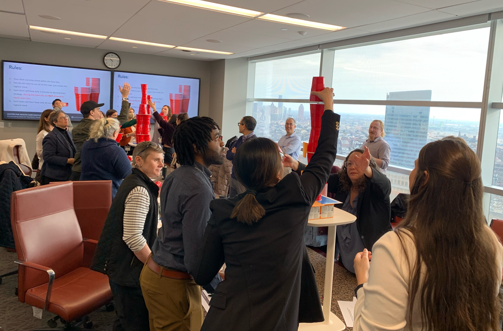 Several teams participate in a problem-solving exercise, stacking red cups on a table, at the Innovation Accelerator Program.
